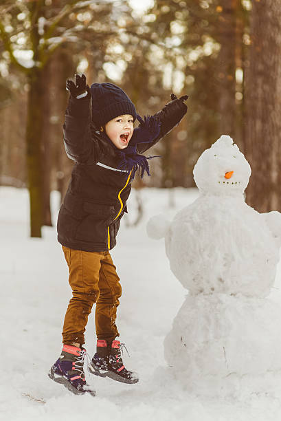 The concept of winter activities . Happy boy making snowman outdoor stock photo