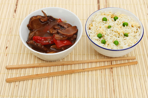 Chinese meal, duck in plum sauce and egg fried rice in bowls with chopsticks on a bamboo matt
