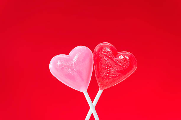 istock Pair of heart shaped lollipops hugging against a red background 508028546