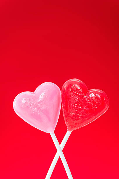 istock Pair of heart shaped lollipops hugging against a red background 508029308