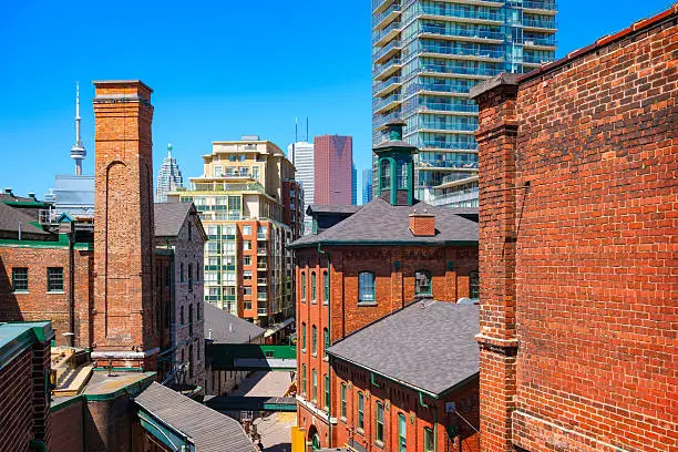 Photo of old brick towers of the chic Distillery District with new condos and downtown skyscrapers in the background in Toronto, Ontario, Canada.