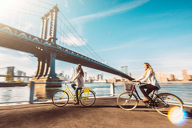 Two girl friends riding their bicycles along The East River in New York City.