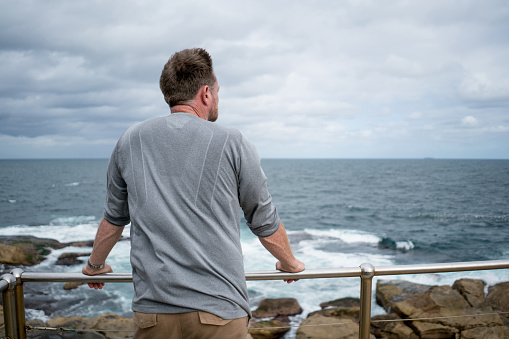 Thoughtful adult man at the beach on a cliff looking at the ocean