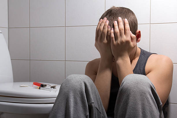 stoned man with heroin addiction sitting in bathroom stock photo