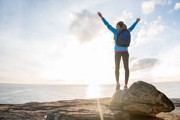 Happy hiker reaching the top Happy hiker reaching the top of a mountain and standing with arms up watching the sunset travel destinations 20s adult adventure stock pictures, royalty-free photos & images