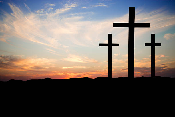 Easter. The crucifixion. Three wooden crosses in silhouette stand silently on a hill at sunset. The dramatic sky is beautiful in its blue and orange colors. Christianity, religious themes. Copyspace.