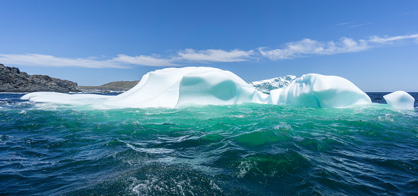 The top of an iceberg is showing as it floats in the North Atlantic Ocean, with Quirpon Island in the background, a part of Newfoundland Canada.