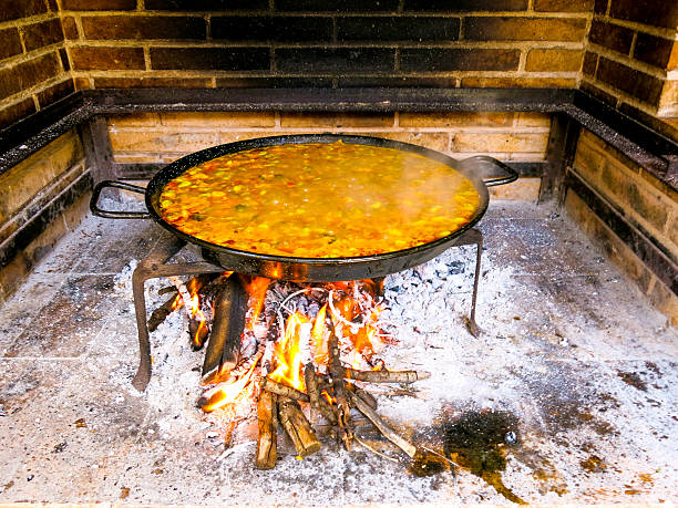 A pork and vegetable paella cooks slowly over an open wood fire in an outside kitchen in the town of Elche, Spain.
