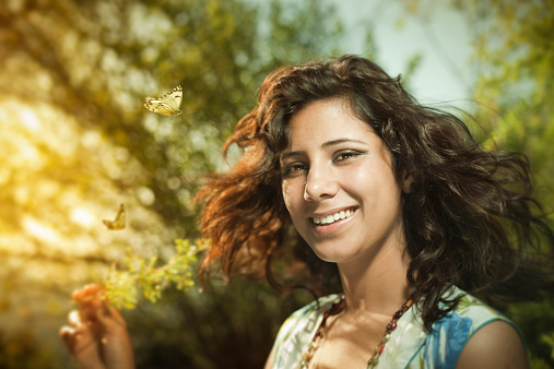 Close-up of beautiful, Happy, young woman in sunshine nature with foliage and butterflies. She is holding a plant twig.