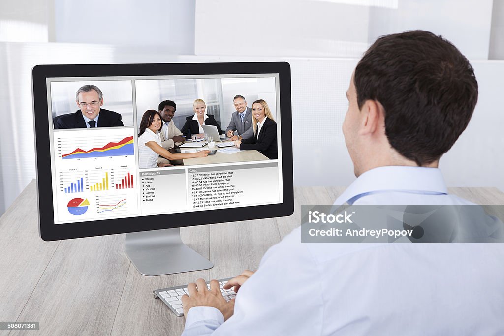 Uomo d'affari le videoconferenze con i colleghi al computer alla reception - Foto stock royalty-free di Inquadratura da sopra le spalle