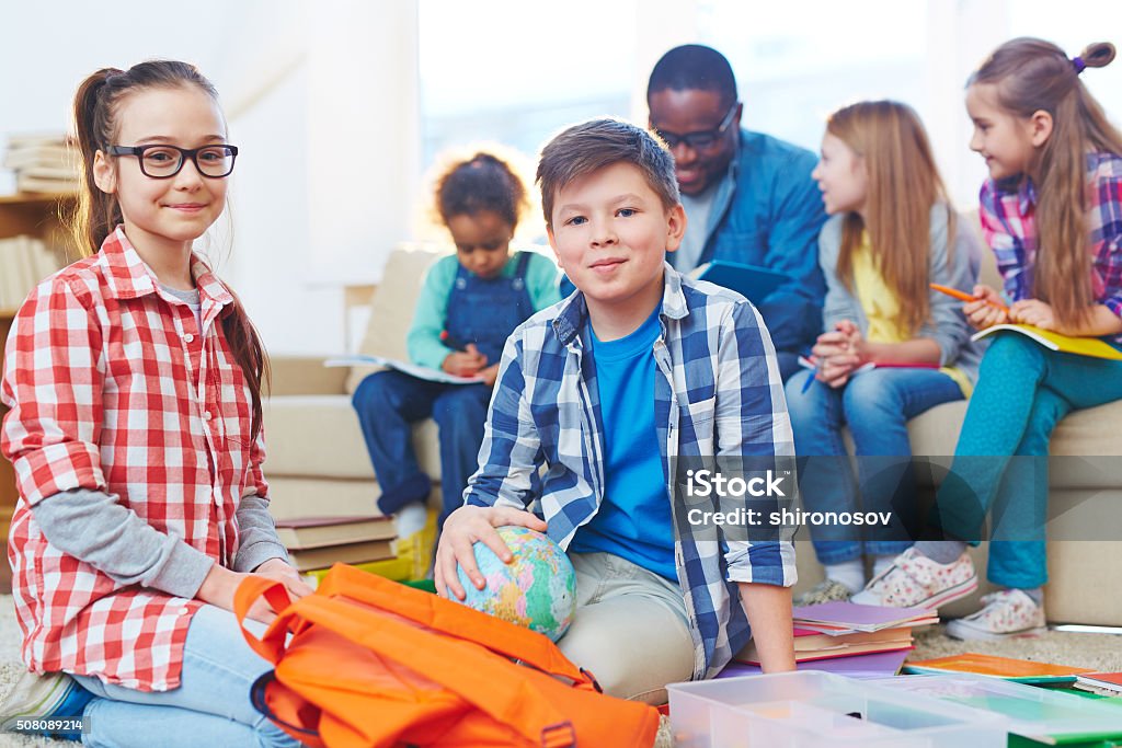 Cute preschoolers Little boy and girl looking at camera on background of teacher and other children Adult Stock Photo