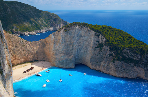 Yachts & pleasure boats moored in the turquoise waters just off Shipwreck Beach of Zakynthos. To the locals it's known as Navagio Beach. Stranded on the sand is the wreck of the Panagiotis (originally built in Scotland in 1937, and called the Saint Bedan), wrecked in 1980 and possibly engaged in nefarious, smuggler-type activities.