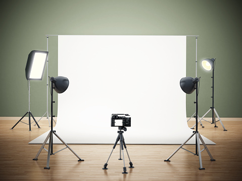 Photographic studio with camera standing on the tripod and lighting equipment