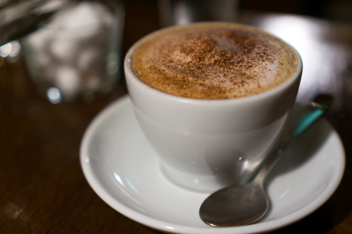 A small cup of cappucino on a coffee table in a cafe.