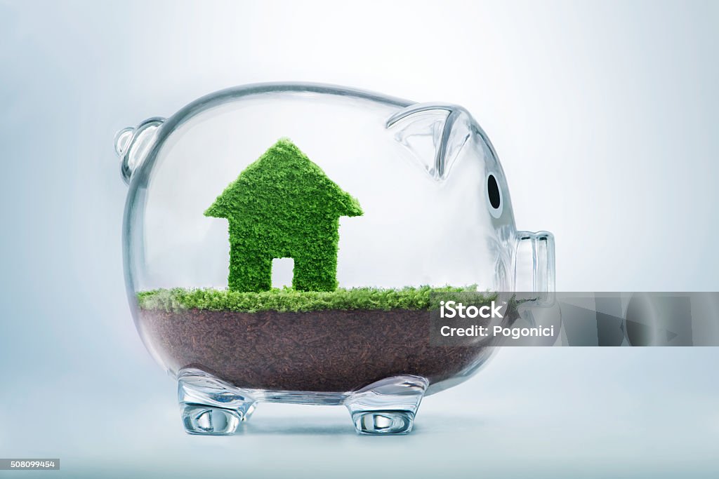 Saving to buy a house or home savings concept Saving to buy a house or home savings concept with grass growing in shape of house inside transparent piggy bank Investment Stock Photo