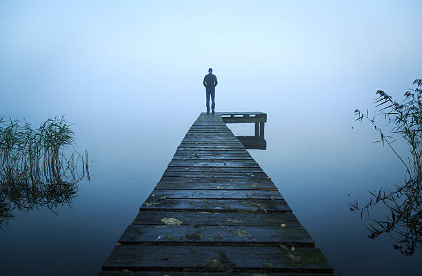 Alone on a jetty Depressed man standing alone on a jetty on a foggy autumn day. grief stock pictures, royalty-free photos & images