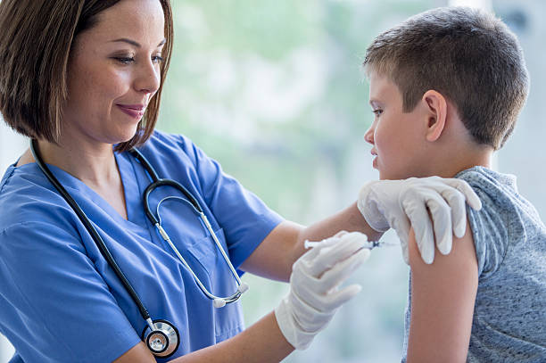 Little Boy Getting a Vaccine A nurse is giving a elementary age boy a flu shot at the doctor's office. injecting flu virus vaccination child stock pictures, royalty-free photos & images