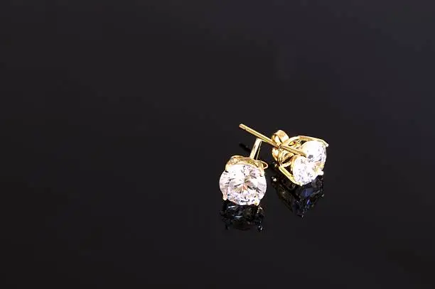 Gold stud diamond earrings on black background.