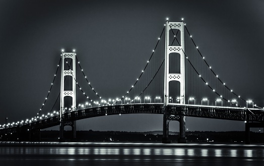  The Mackinaw Bridge spans the straits between the Upper and Lower Peninsula of Michigan. Shot at night with illumination reflecting in the waters of the Great Lakes.