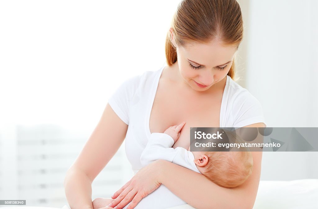 mother breastfeeding newborn baby in white bed mother breastfeeding her newborn baby in a white bed Breastfeeding Stock Photo