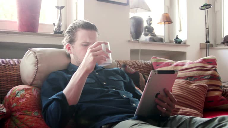 Man drinking coffee and reading on his tablet