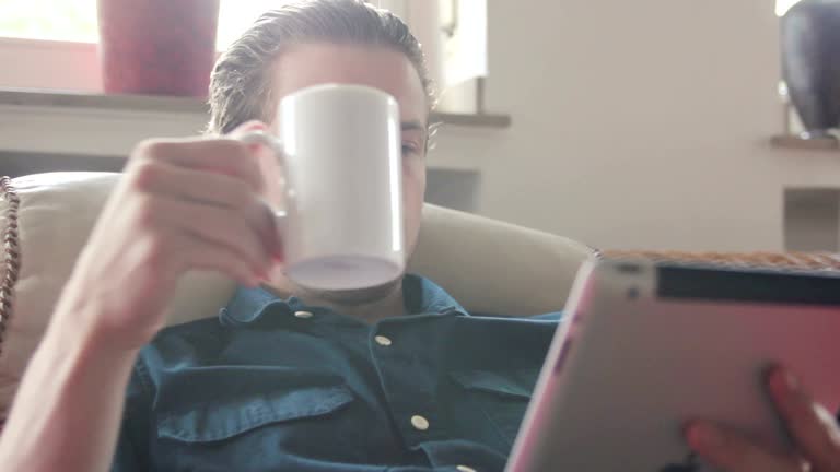 Man reading an article on his tablet and drinking tea