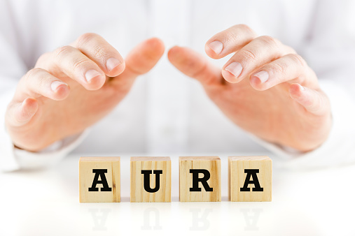 Word - Aura - on wooden cubes with a man in a white shirt holding his hands cupped protectively over the top in an inspirational and spiritual concept.
