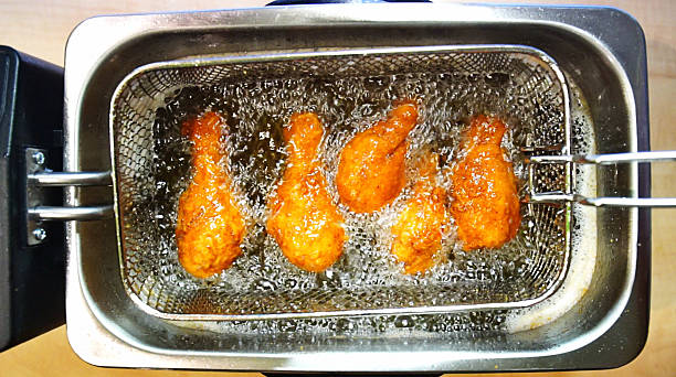 Frying chicken. Closeup top view of several pieces of chicken being fried in a stainless steel deep fryer. Sparkling and greasy chicken thighs. deep fried photos stock pictures, royalty-free photos & images