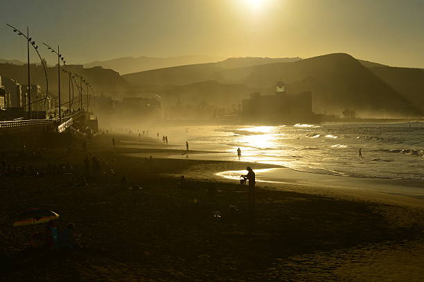 Gran Canaria, Spain, - December 18, 2015: Tourists and local people enjoying the Winter sun, swimming and surfing in the sea. The islands capital city Las Palmas De Gran Canaria is built right up to beach called Playa De Canteras with the Auditorio concert building at the South end.