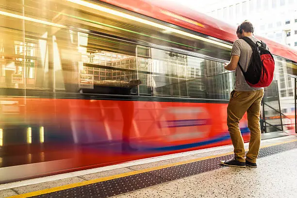 Photo of Young man with backpack and headphones waiting for train