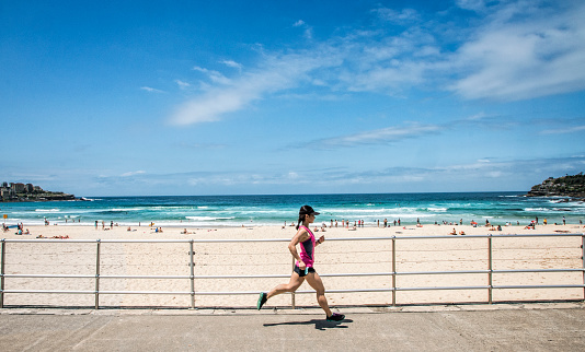 Young woman running on the sidewalk next at Bondi Beach, Sydney Australia.