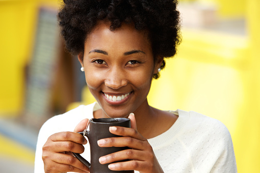Close up portrait of a beautiful african american woman smiling with cup of a coffee