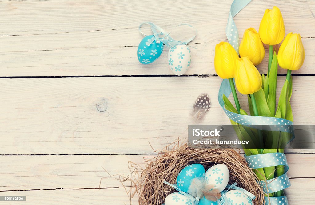 Easter eggs in nest and yellow tulips Easter background with blue and white eggs in nest and yellow tulips. Top view with copy space. Vintage toned Easter Stock Photo