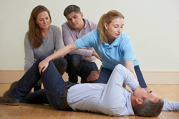 Woman Demonstrating Recovery Position In First Aid Training Clas stock photo