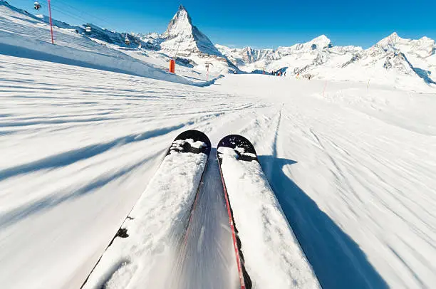 Motion blur in the foreground as a skier descends a piste in the Swiss resort of Zermatt in the Alps, with the peak of the Matterhorn in the distance.