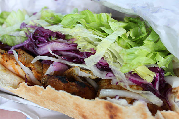 Photo showing a tasty chicken shish kebab / kebob, in an open, griddled pitta bread with shredded lettuce, onion, red cabbage and marinated pieces of chicken, drizzled in a chili sauce.  This healthy takeaway was purchased from a local Turkish fast-food restaurant.