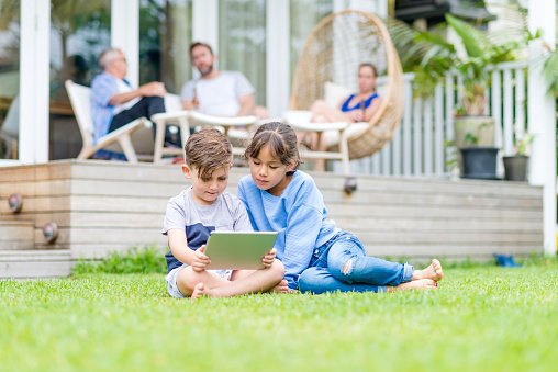 Grandfather, father and mother talking to each other, children using a digital tablet on the grass.