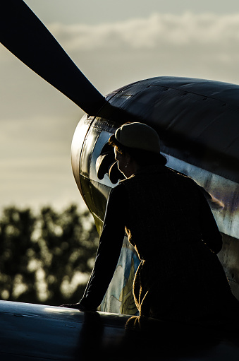 Goodwood, Sussex, UK - September 12, 2015. A female in period costume sits on the wing of a 1940s fighter aircraft.