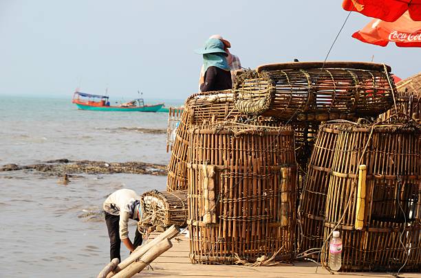 Stacked baskets at crab market in Kep KEP, CAMBODIA - February 3, 2015: Fishermen working and sitting at waterfront, stacked fishing baskets on February, 3, 2015 in Kep, Cambodia kep stock pictures, royalty-free photos & images