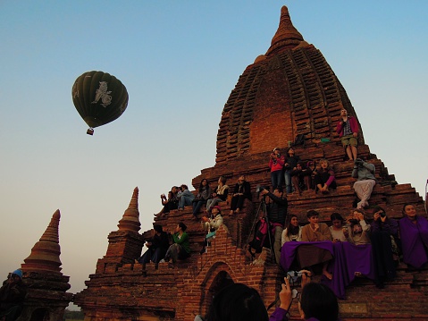 Bagan, Myanmar - February 22, 2015: People are sitting on the stairs of an ancient temple, in the background a hot-air ballon in the sky on February, 22, 2015 in Bagan, Myanmar