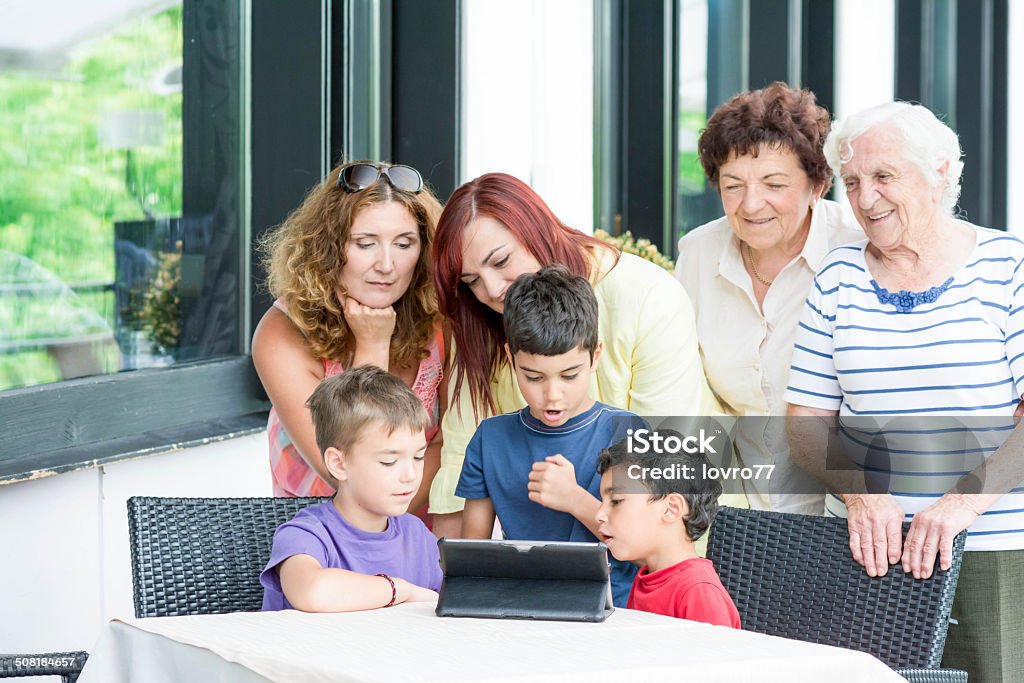 Kids looking on digital tablet Kids looking on digital tablet in restaurant. Behind two mother talking. Adult Stock Photo