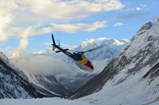 MANASLU-TREK, HIMALAYAS, NEPAL  - October 20, 2014: A red, yellow and blue helicopter flying in the air between mountains on October, 23, 2014 on the Manaslu-trek in the Himalayas, Nepal