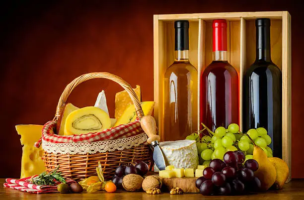 Three bottles of wine with basket cheese, grapes and food in still life