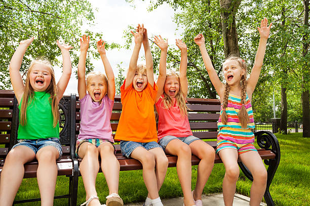 istock Happy children with arms and sit in row on bench 508201363