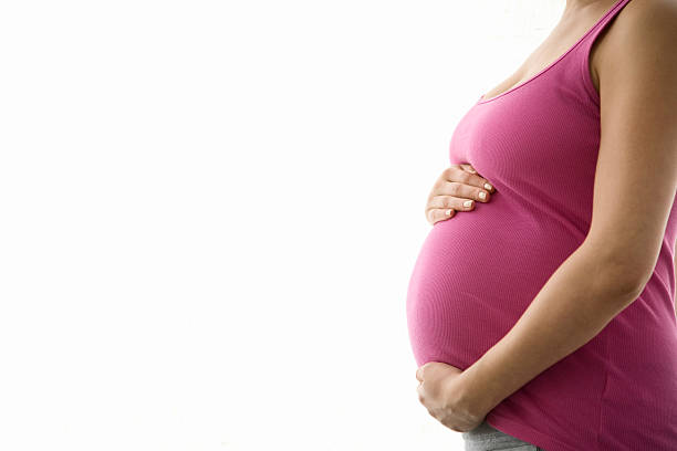 vue de côté de la partie médiane de femme enceinte avec mains tenant ventre - herne bay photos et images de collection