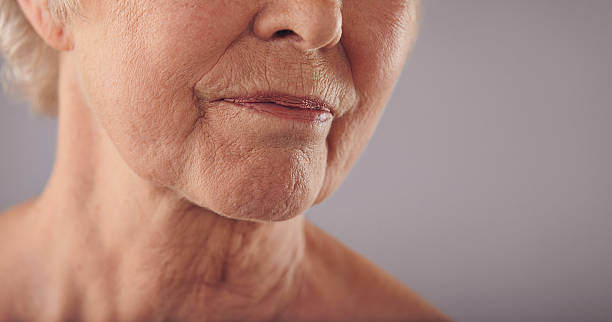 Senior female face with wrinkled skin Macro of a senior female face with wrinkled skin against grey background. Cropped old woman face. wrinkled stock pictures, royalty-free photos & images