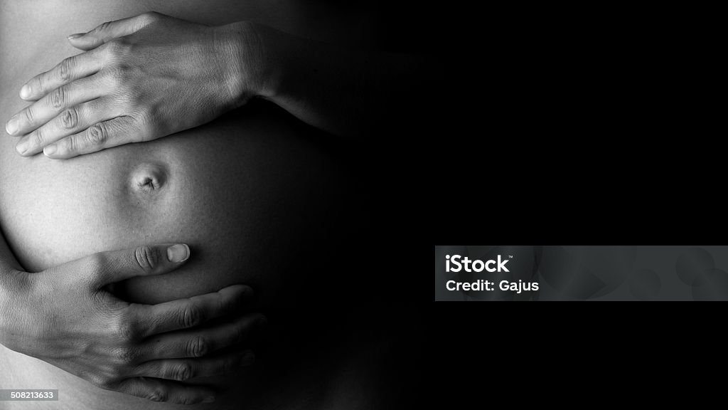 Expectant mother holding her belly, in low-key Artistic black and white close-up of an expectant mother holding her belly, concept of care, health and pregnancy, in low-key, with copy space on black. Pregnant Stock Photo
