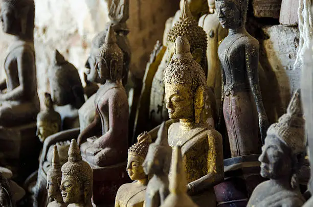 several diverse buddhas standing in a group. A golden one sticking out of the crowd, location: cave in Laos