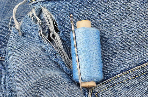 Threads and needle on jeans backround, wear repair concept