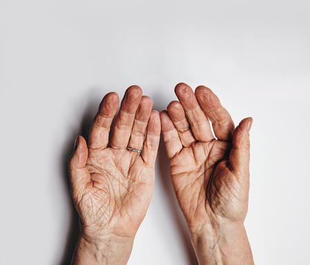 Top view of two empty female hands over grey background. Senior woman hands pleading. Wrinkled palms of aged woman with copy space.